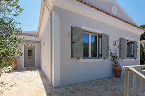 Ein weißes Gebäude mit grünen Fensterläden, einem gepflasterten Eingangsbereich und einem Blumentopf.