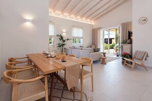 A spacious living area with a wooden dining table, wicker chairs, a sofa, and a television.