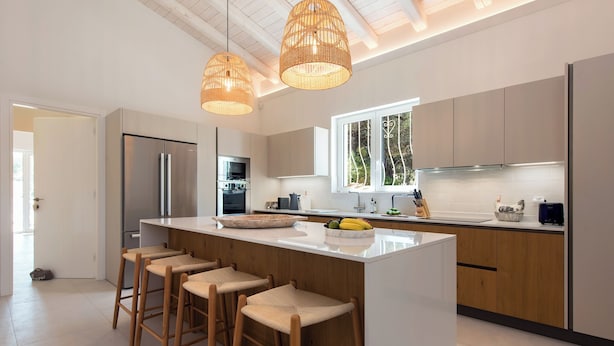 Une cuisine moderne dotée d’un îlot central, de tabourets de bar, d’appareils électroménagers en acier inoxydable et de luminaires suspendus.