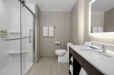 Un bagno moderno con box doccia in vetro, un water, un lavandino con specchio e un portasciugamani.. Holiday Inn Express & Suites WOODSIDE LAGUARDIA AIRPORT by IHG