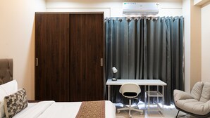 Un dormitorio con cama, escritorio, silla, armario y aire acondicionado.