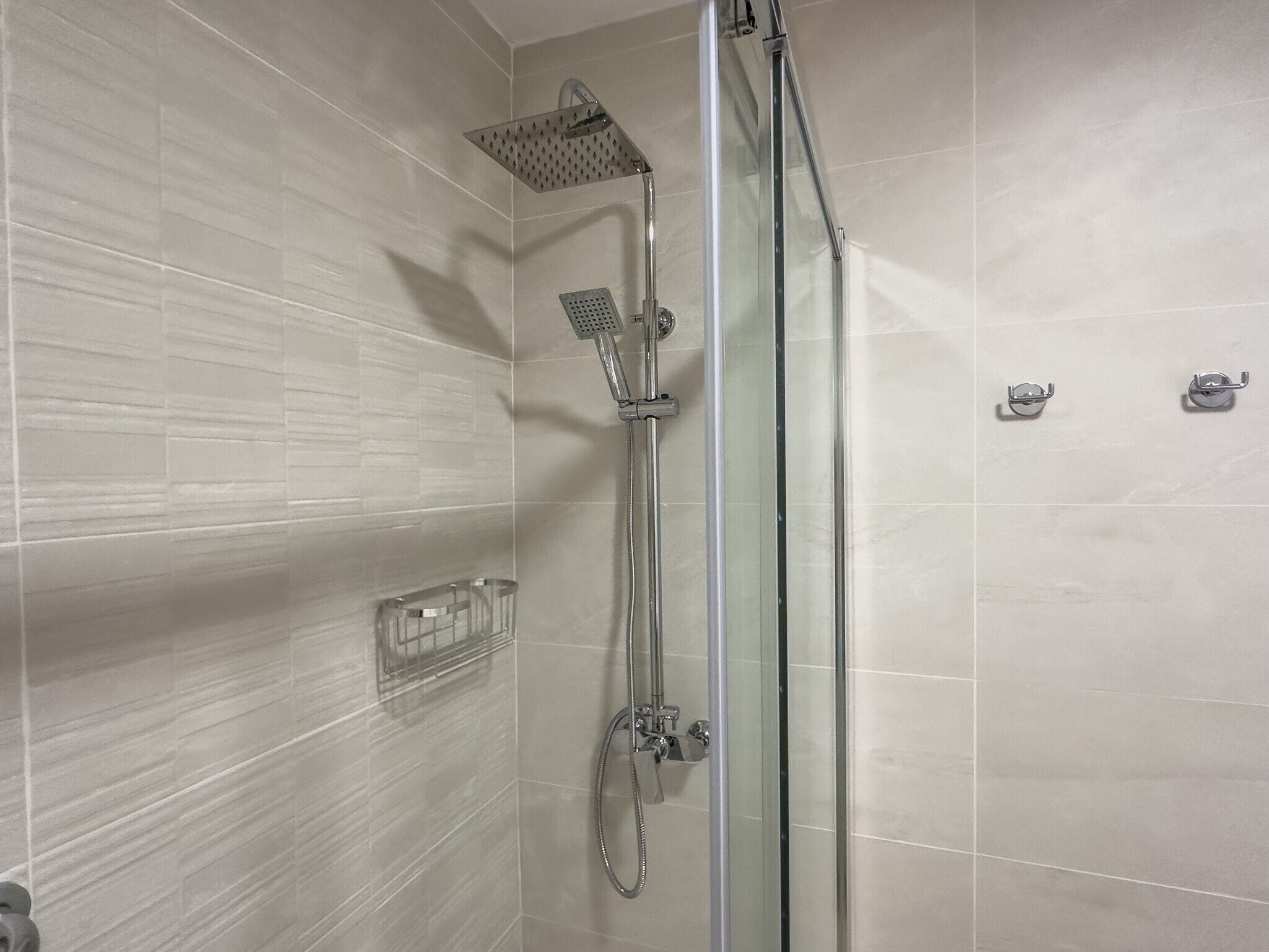 A shower with a glass door, a handheld showerhead, and a wall-mounted faucet.