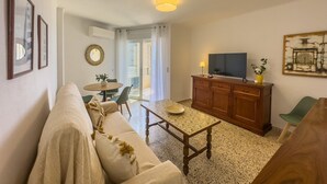 A living room with a sofa, a table, a television, a cabinet, and a balcony door.