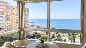 A balcony with a view of the sea, a table with a plant, and a chair.