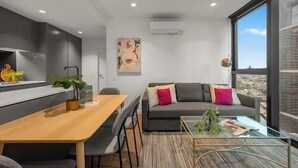A modern living space with a dining area, a sofa with cushions, and a large window offering a view.