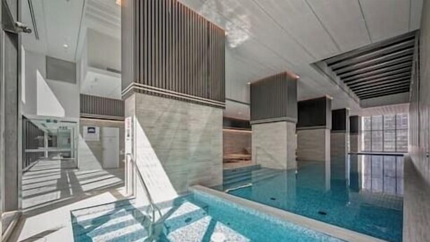 A modern indoor swimming pool with clear water, a tiled floor, and a glass barrier.