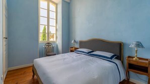 A bedroom with a bed, a nightstand, a lamp, a chair, and a window. - Property XVIII of 500 m2 with private pool and park 20 minutes from Bordeaux. (Virsac)