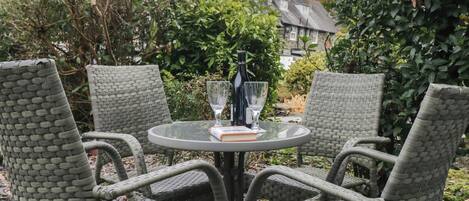 A round glass table with wicker chairs, a bottle, and two wine glasses.