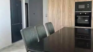 Un espace repas moderne avec une table en bois foncé et quatre chaises, un four encastré et un mur recouvert de panneaux en bois.