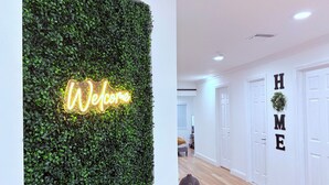 Een modern interieur met een groene wand met een ‘Welcome’-bord, een hal met houten vloer en witte deuren met de tekst ‘HOME’.