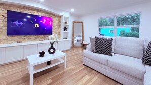 Een moderne woonkamer met een flatscreen televisie, een witte bank, een salontafel en een groot raam met uitzicht.