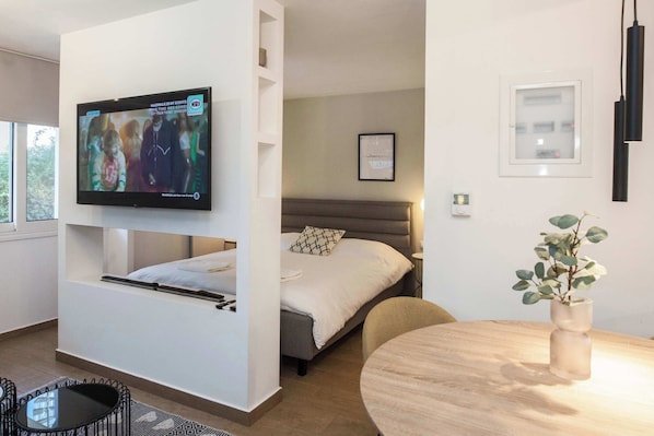 Une chambre d’hôtel moderne, équipée d’un lit, d’un téléviseur fixé au mur, d’une petite table et d’une plante.