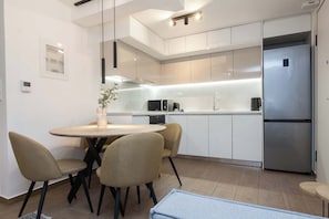 Une cuisine moderne avec des meubles blancs, un réfrigérateur en acier inoxydable, une table à manger avec des chaises et une petite plante posée sur le comptoir.