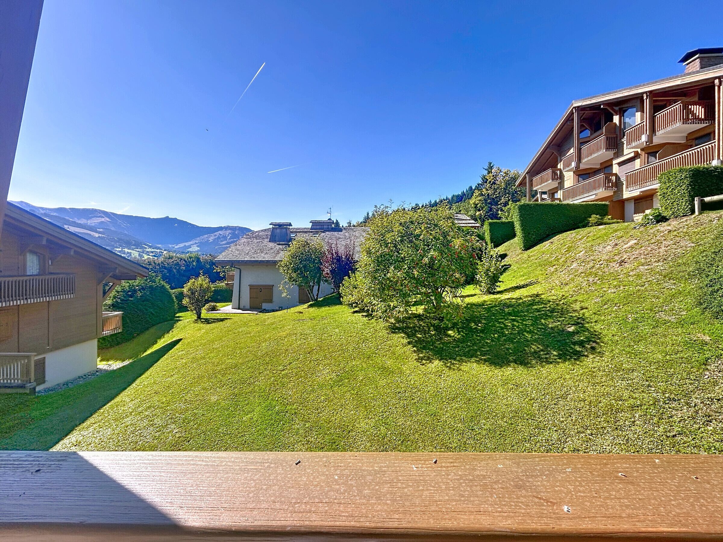 Vue sur un quartier résidentiel depuis une colline, avec des maisons, une terrasse en bois et des montagnes en arrière-plan.