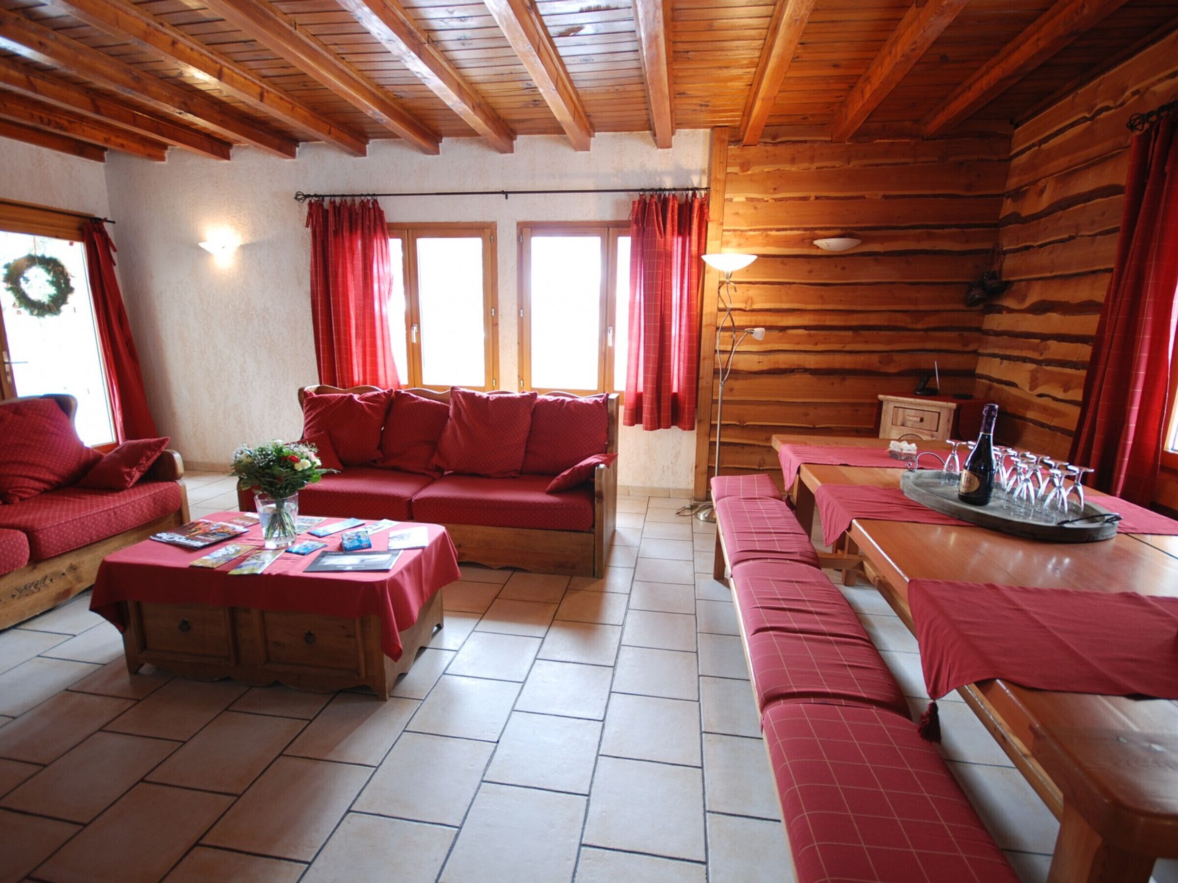 A cozy log cabin interior with a red sofa, wooden benches, a dining table, and a fireplace.
