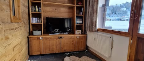 Un meuble de rangement en bois comprenant un téléviseur, des étagères et une fenêtre donnant sur un paysage enneigé.