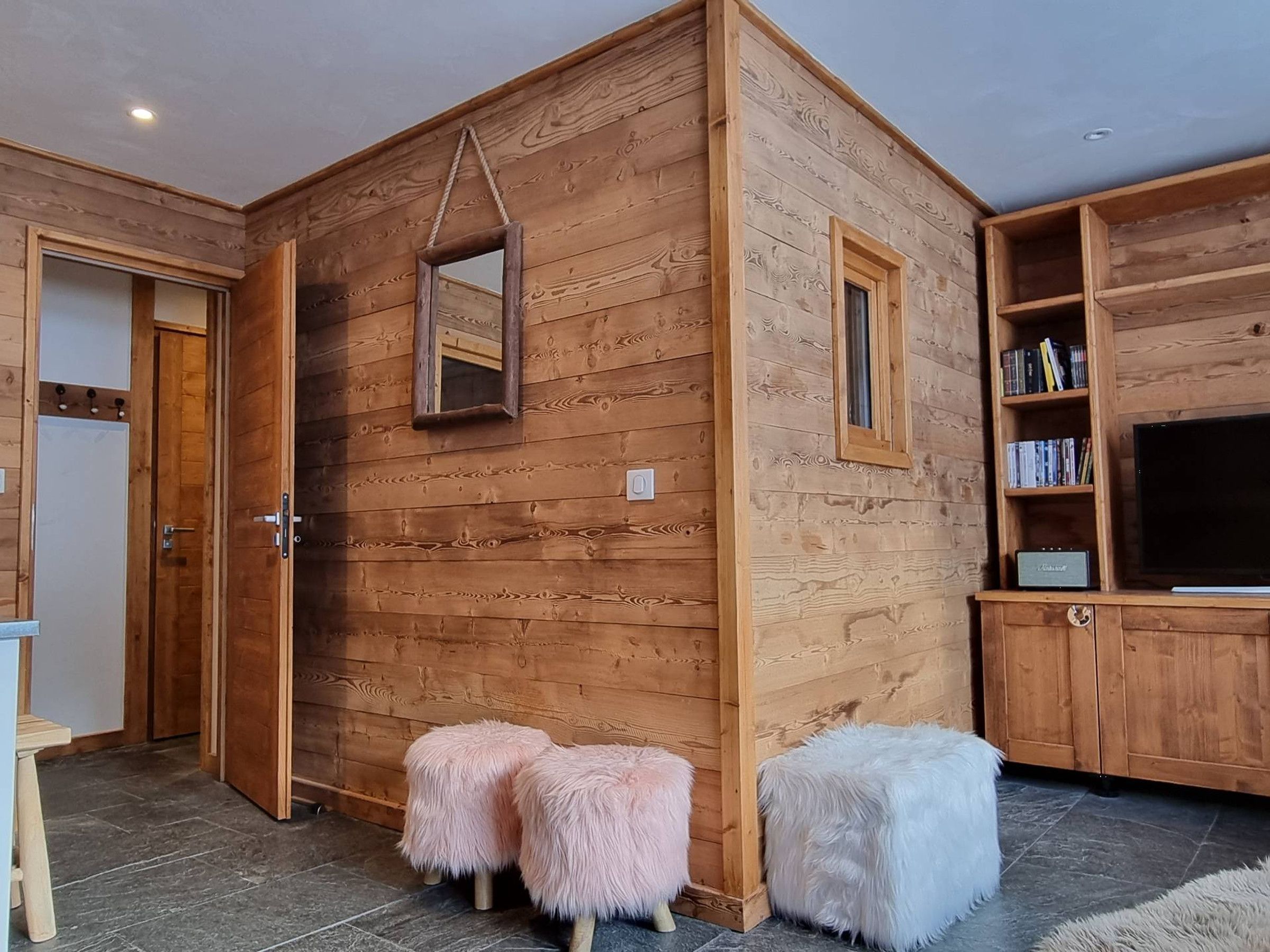 A wooden interior with a TV, bookshelves, and two fluffy stools.