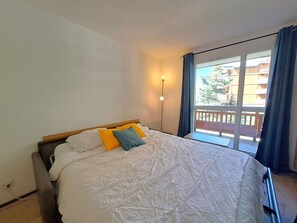 Ein Schlafzimmer mit Bett, Nachttisch, Lampe und Blick auf den Außenbalkon.