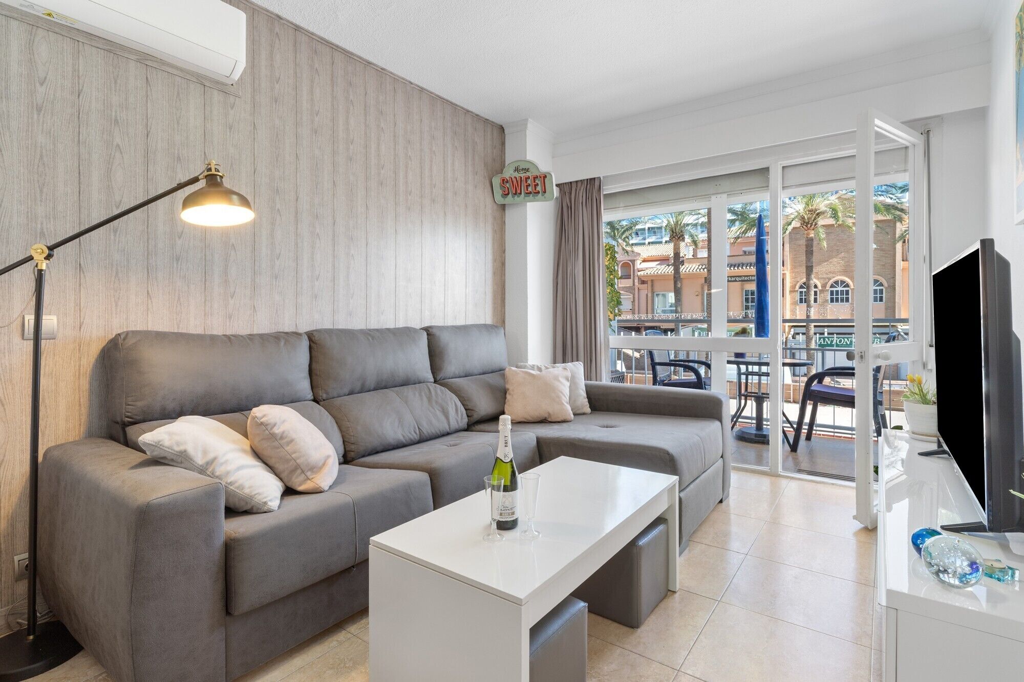 A modern living room with a grey sofa, a white coffee table, a TV, and a view of the outside.