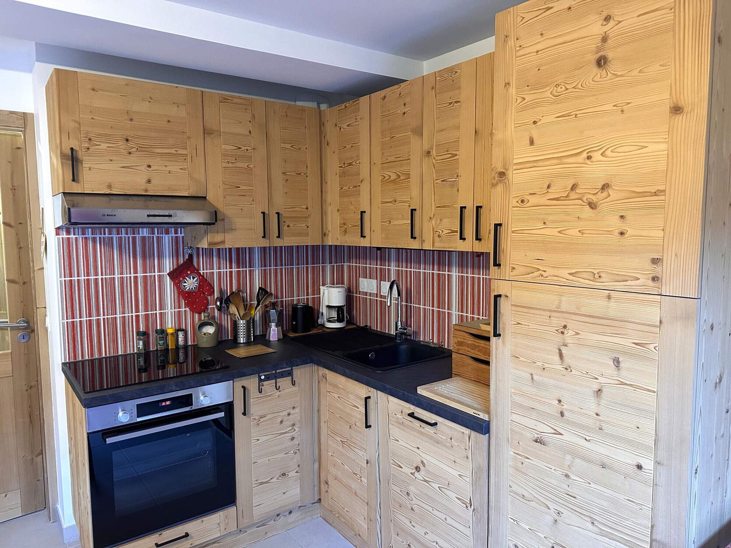 A kitchen with wooden cabinets, a Bosch oven, a striped backsplash, and a coffee maker.