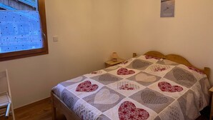 A bedroom with a wooden bed, a quilt with heart patterns, a chandelier, a window with a view of a house, and a sign on the wall.
