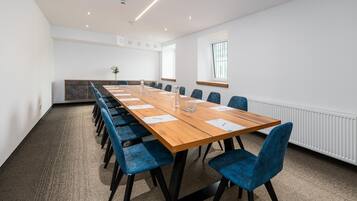 Un salón de conferencias con una larga mesa de madera, sillas tapizadas en azul y una pizarra.