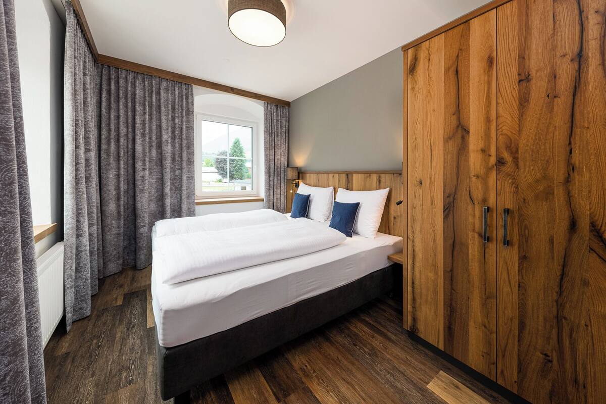 A bedroom with a large bed, wooden wardrobe, and a window with curtains.