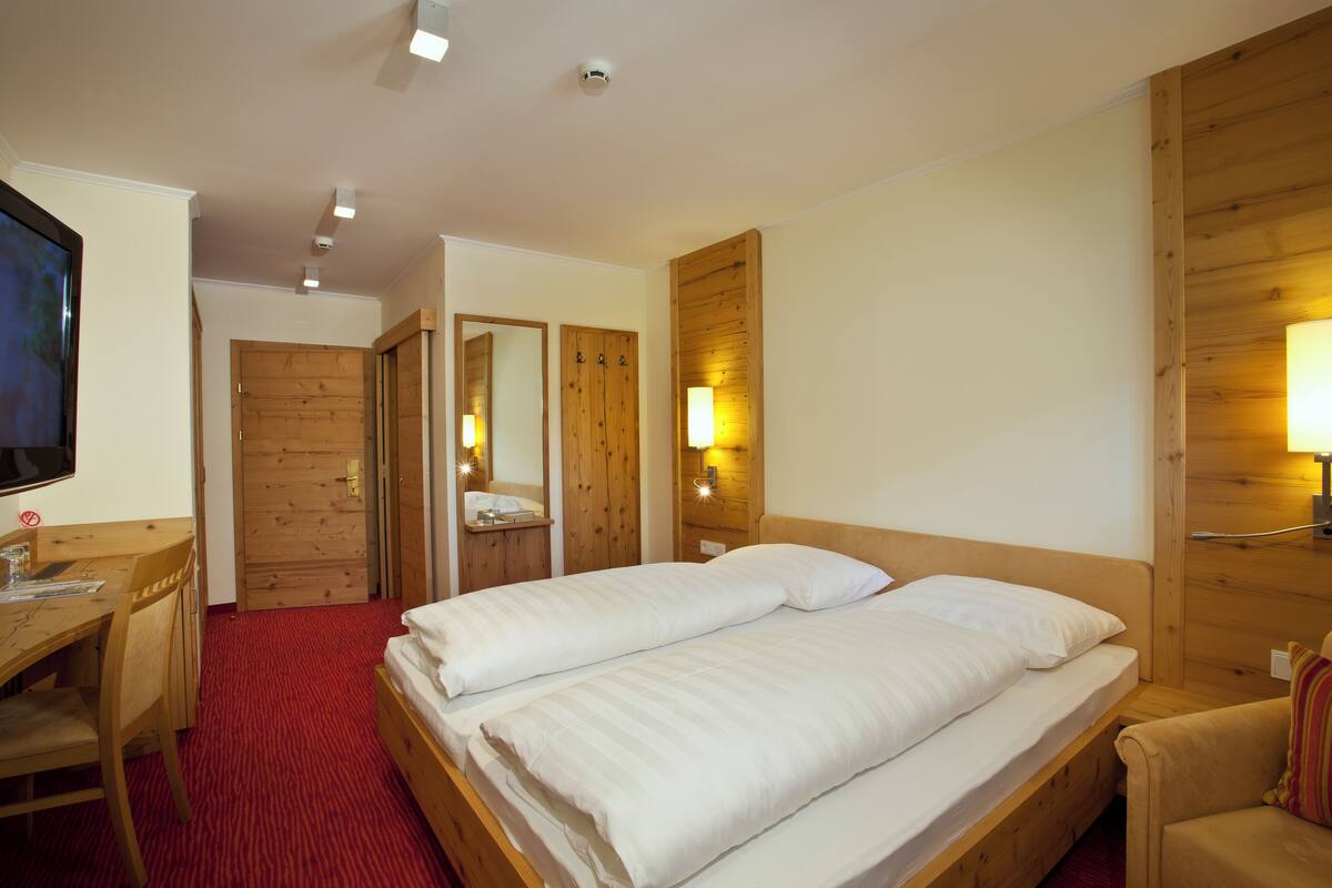 A hotel room with a wooden bed, a desk, a chair, and a television.