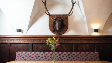Un comedor con un banco de madera, una mesa con un jarrón de flores y una cabeza de ciervo montada en la pared.