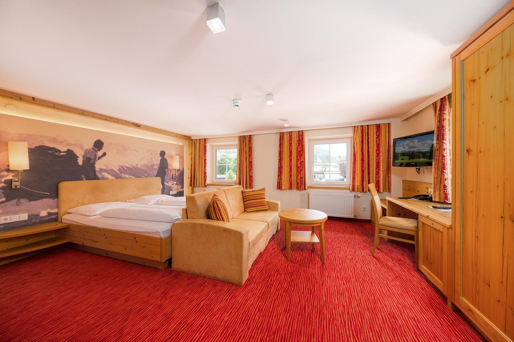 A hotel room with a bed, a sofa, a desk, and a TV.