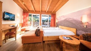 Habitación de cabaña de madera con cama, sofá, escritorio y vistas a las montañas a través de amplias ventanas.