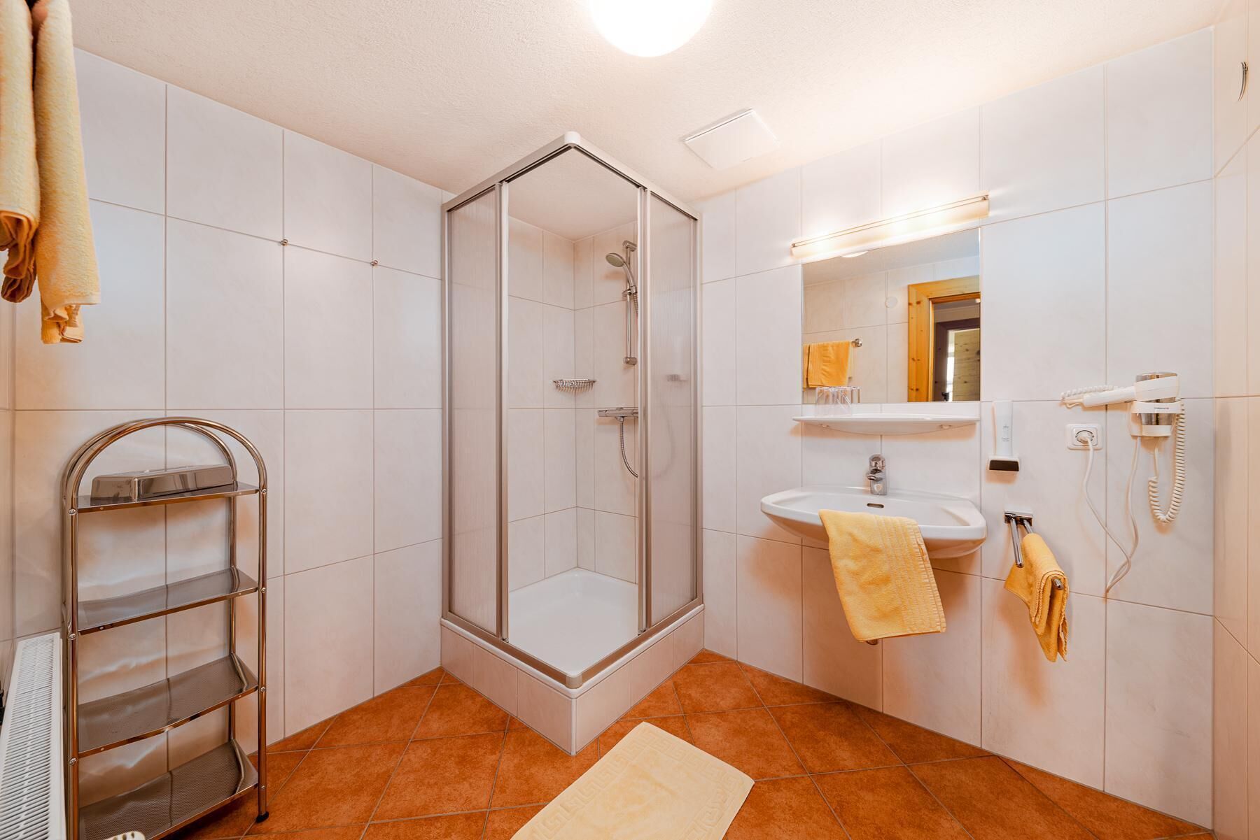 A bathroom with a glass shower enclosure, a sink with a mirror, and a telephone.