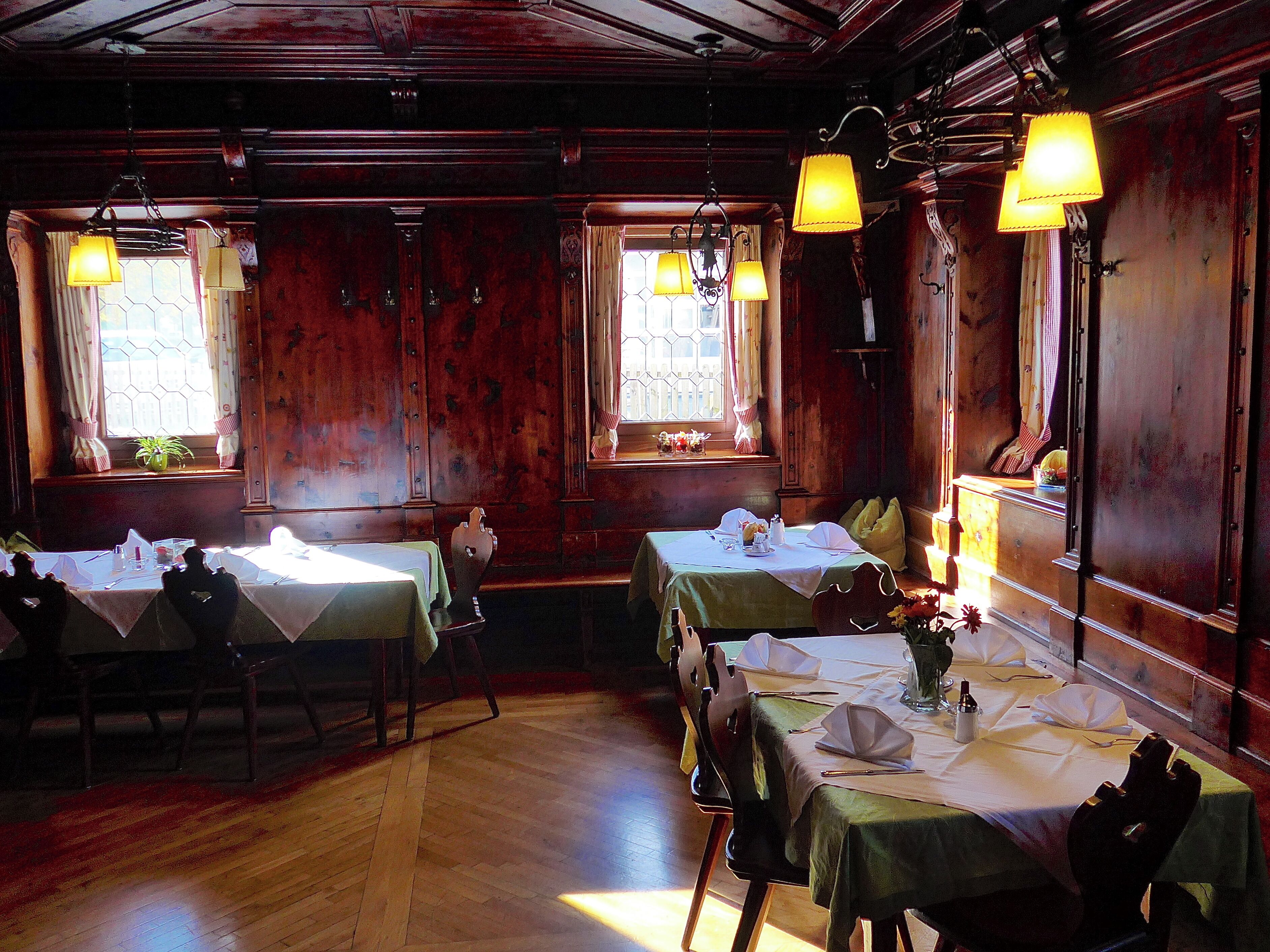 A dining area with wooden walls, multiple tables set for dining, and hanging lamps.