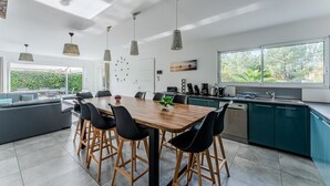 A modern kitchen with a dining area, large windows, and a view of greenery. - Holiday Home in the Heart of the Basin with Pool (Cazaux)
