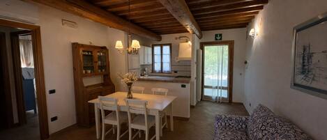 A dining area with a wooden table and chairs, a kitchen with cabinets and a window, and a patterned sofa.