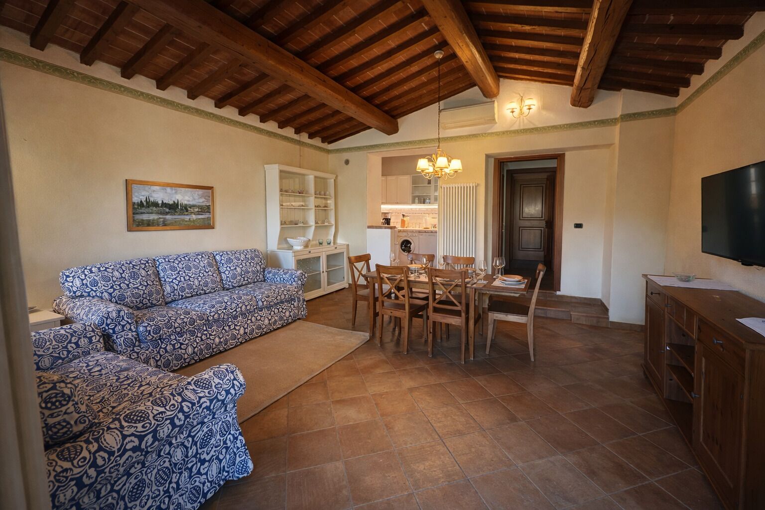 A living room with a sofa, dining table, chairs, a TV, and a kitchen area.