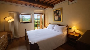 A bedroom with a bed, a nightstand, a lamp, a window with a view, and a radiator. - Agriturismo Borgo Sette Tigli (Montepulciano)