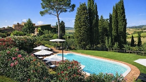 A swimming pool with lounge chairs and umbrellas, surrounded by greenery and tall trees. - Agriturismo Borgo Sette Tigli (Montepulciano)