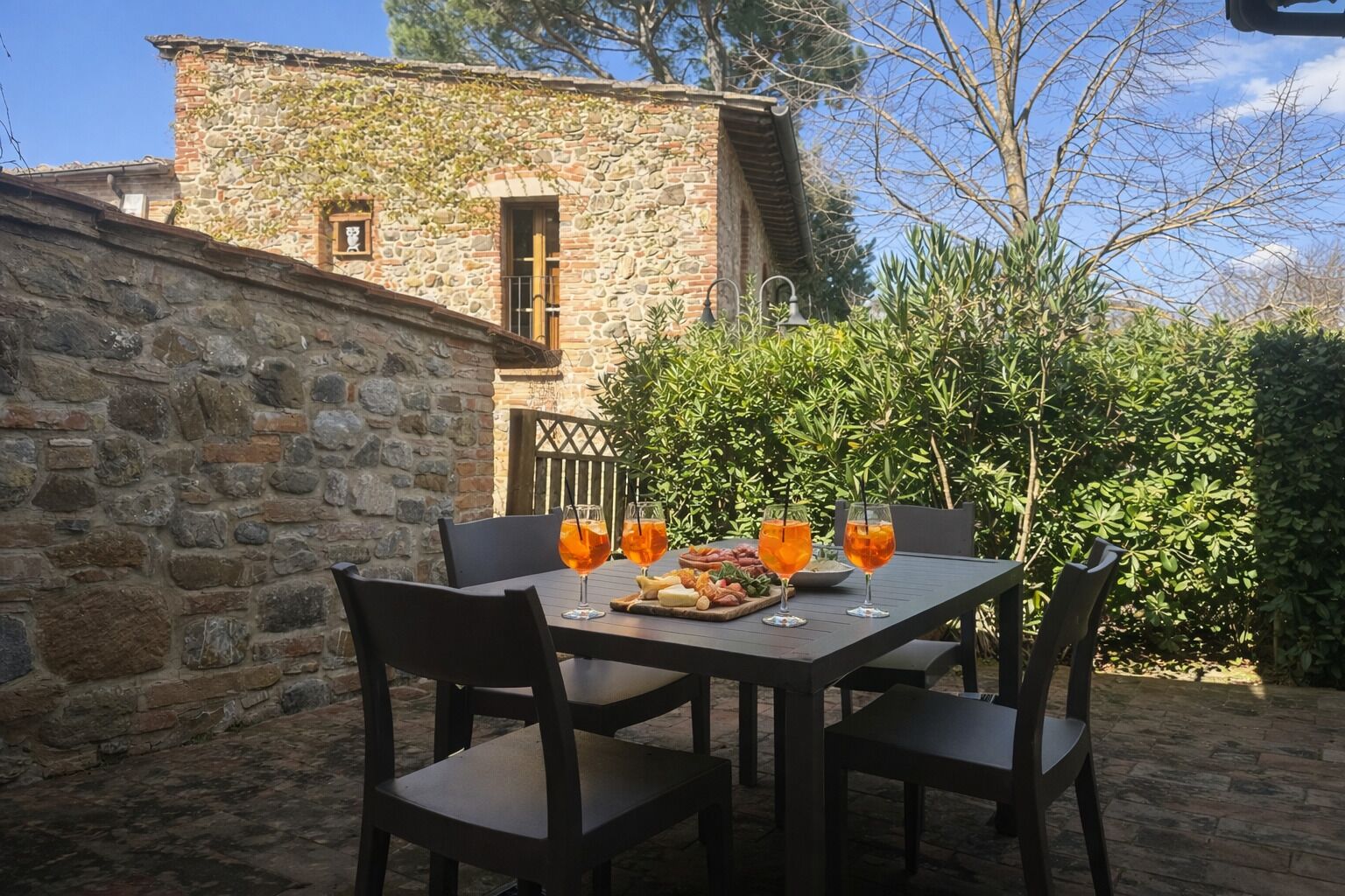 An outdoor dining area with stone walls, a table set with chairs, and a view of a stone building.
