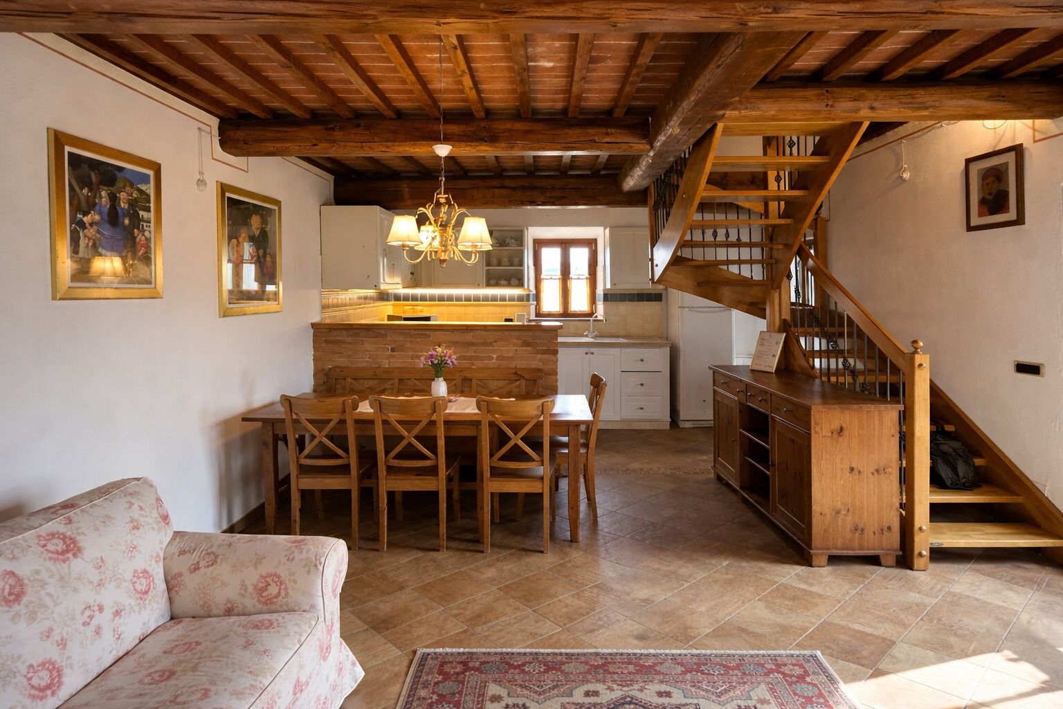 A cozy interior with a dining area, wooden staircase, and a kitchen with a hanging light fixture.