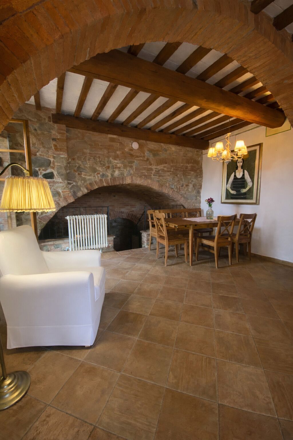 A stone fireplace, wooden beams, a white armchair, and a dining table with chairs.