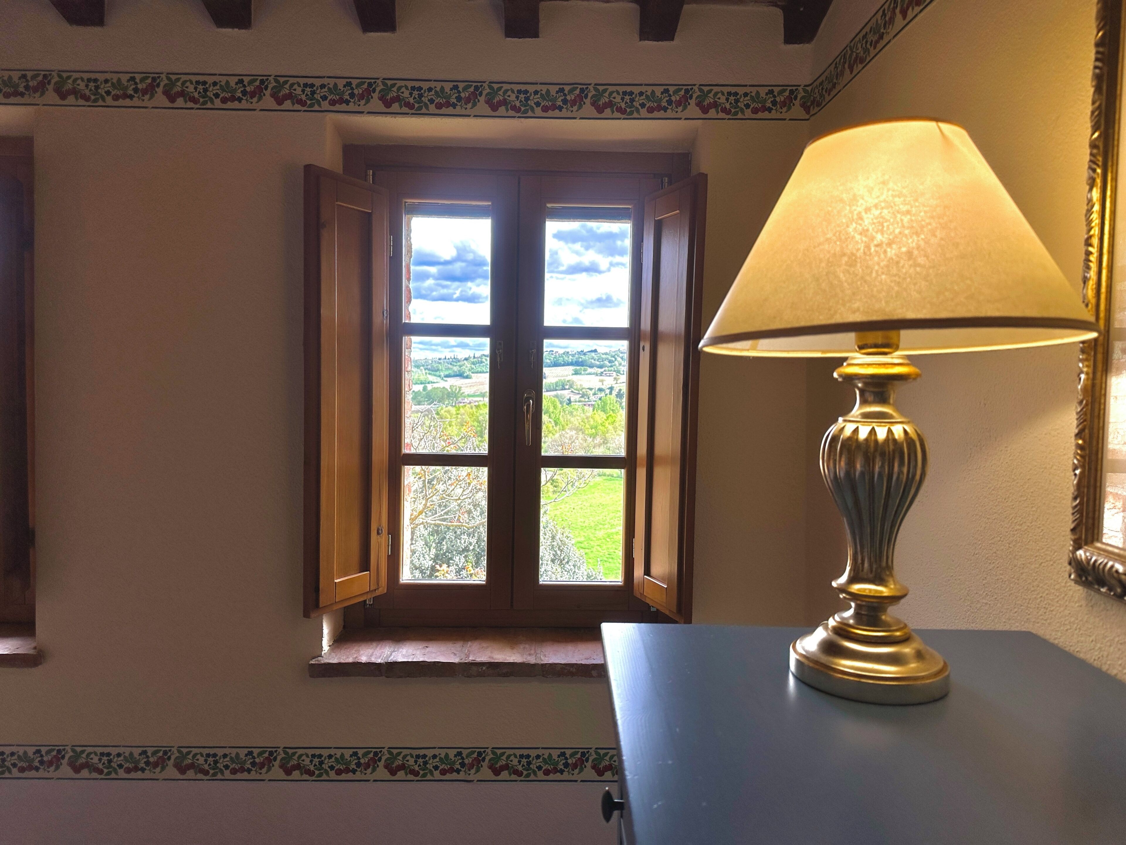 A room with a window, a lamp on a table, and a decorative border on the wall.