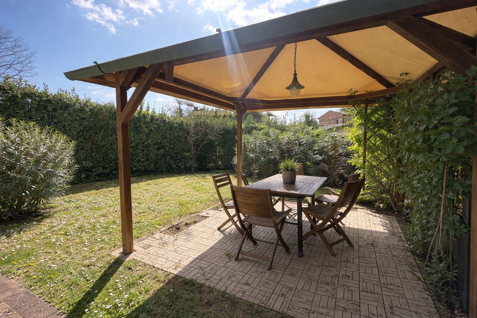 A covered patio with a table and chairs, surrounded by greenery.