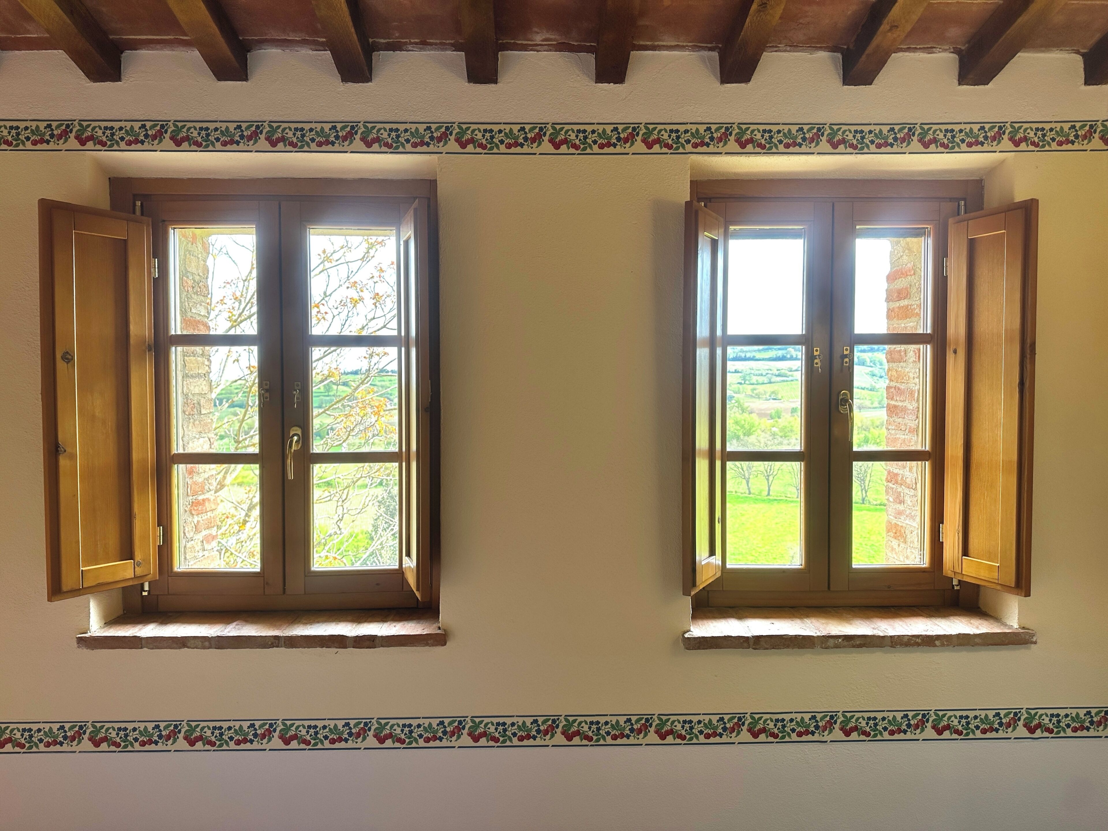 Two windows with open shutters, a wooden ceiling, and a decorative border.