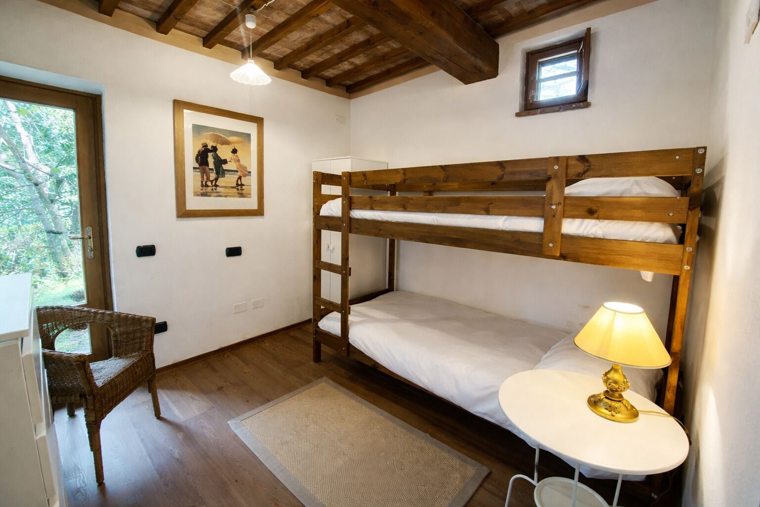 A bunk bed room with a small table and chair, a lamp, and a framed picture on the wall.