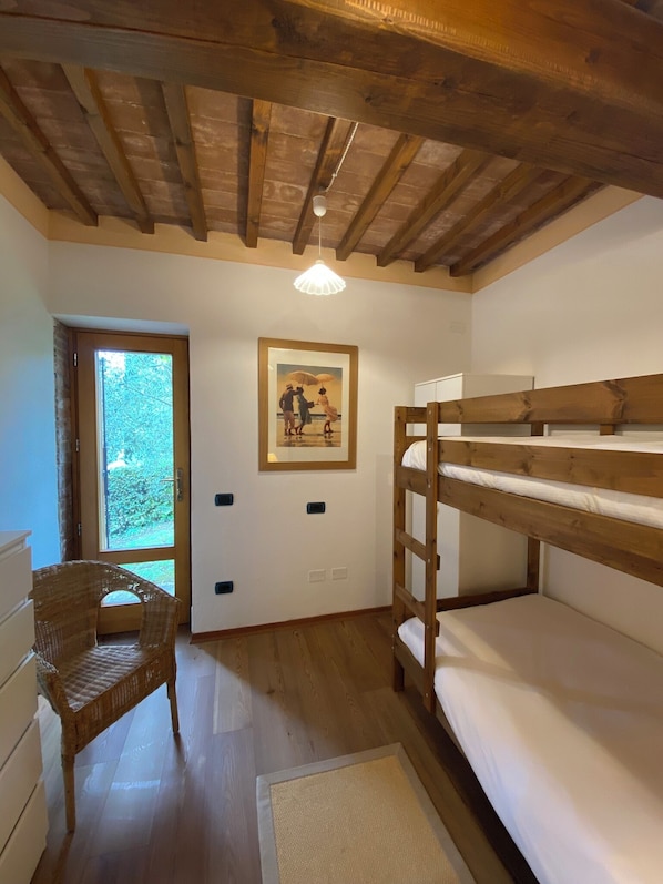 Una habitación con literas, una silla de mimbre, un cuadro en la pared y una puerta que da a un balcón.