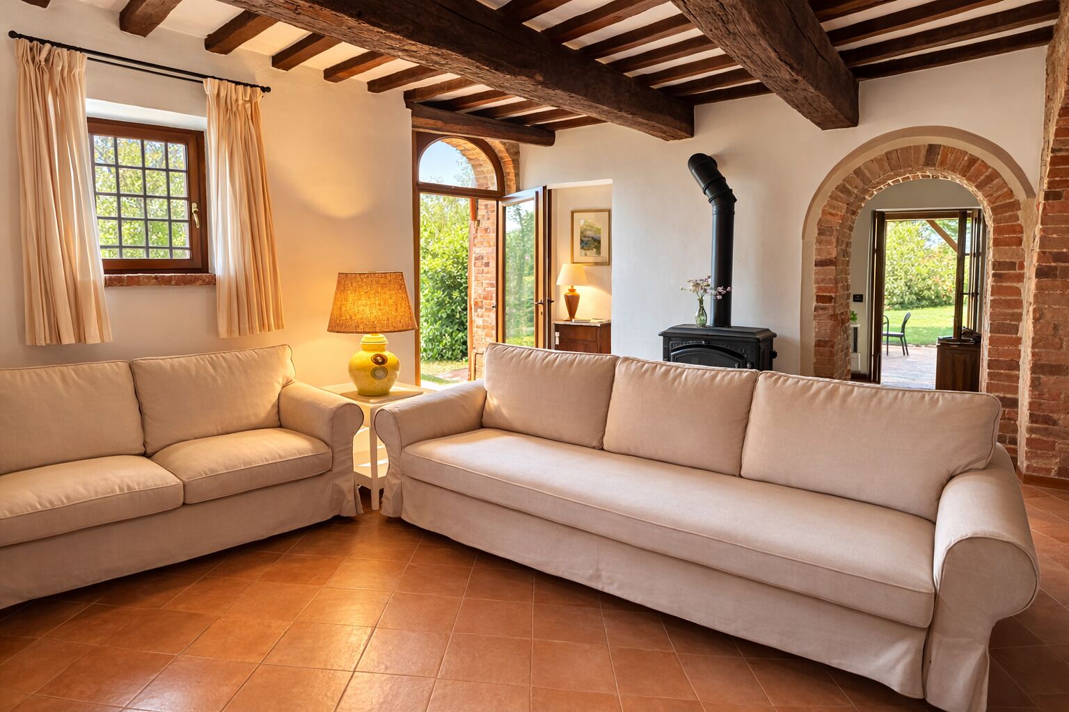 Ein Wohnzimmer mit beigefarbenem Sofa, Holzboden, Kamin und Blick ins Freie.