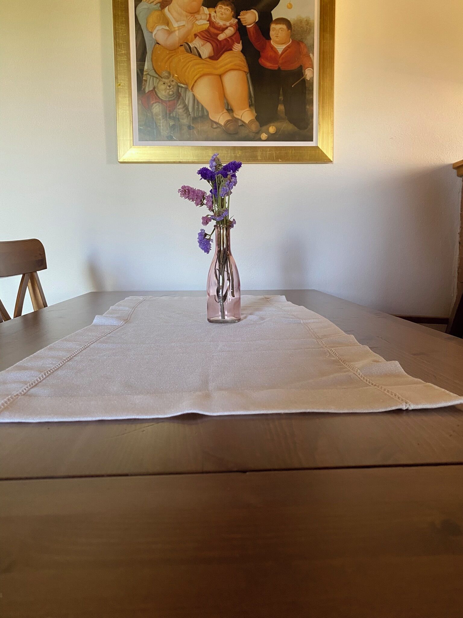 Una mesa con un jarrón de flores moradas sobre un mantel blanco.