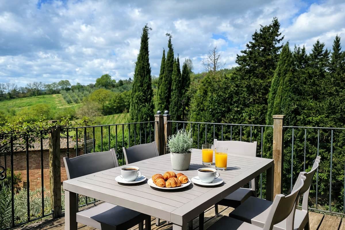 An outdoor dining table with chairs, a potted plant, croissants, coffee cups, and orange juice glasses.