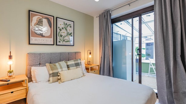 A hotel room with a large bed, two bedside tables, a nightstand, a window with curtains, and two framed pictures on the wall. - Samantha Suite | City 2BR Bungalow Free Parking Garden & WIFI (Cardiff)